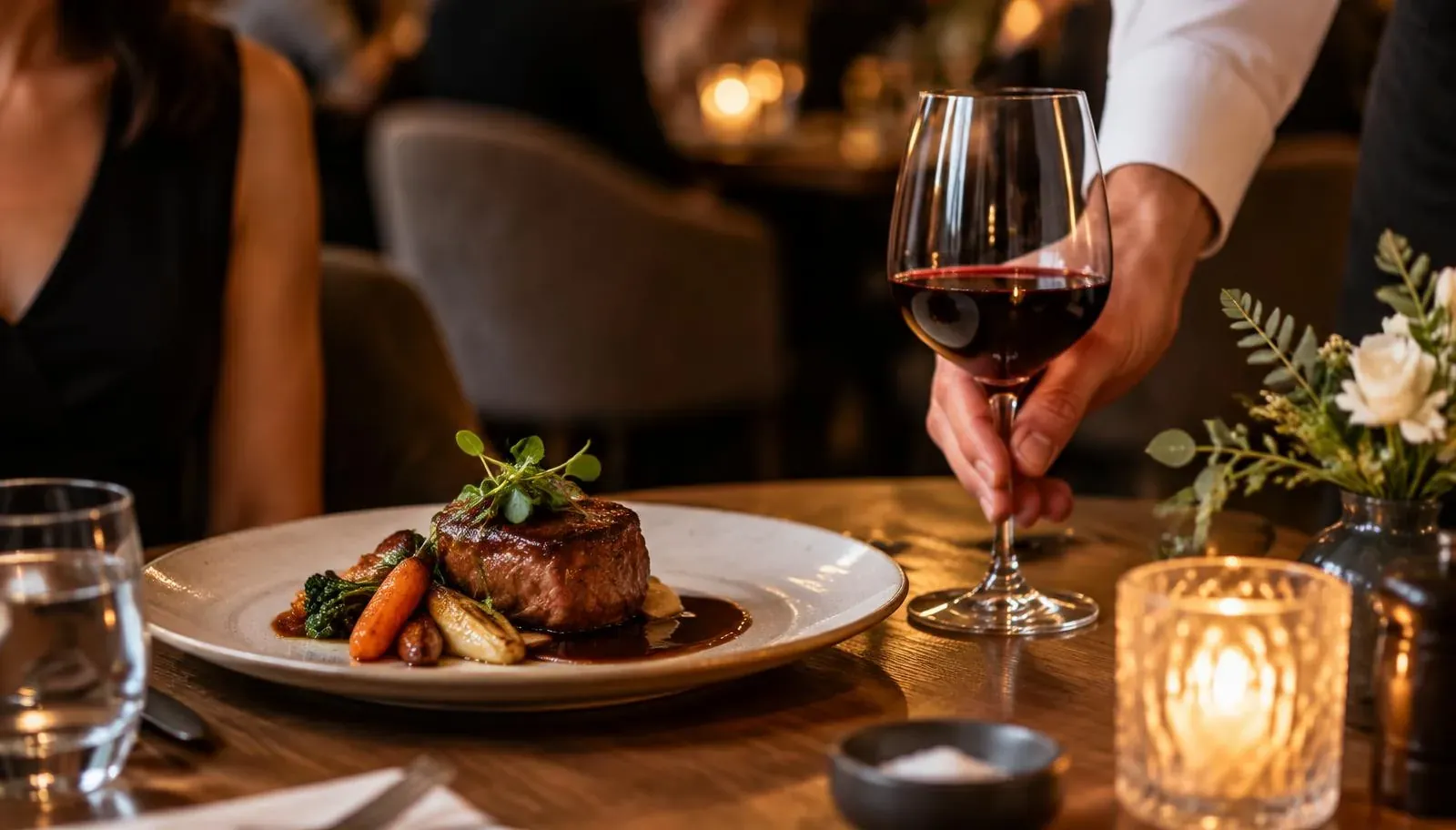 Server placing a glass of wine next to a main course at a restaurant table